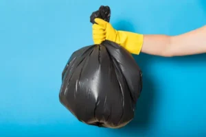 Cleaning gloves holding black trash bag